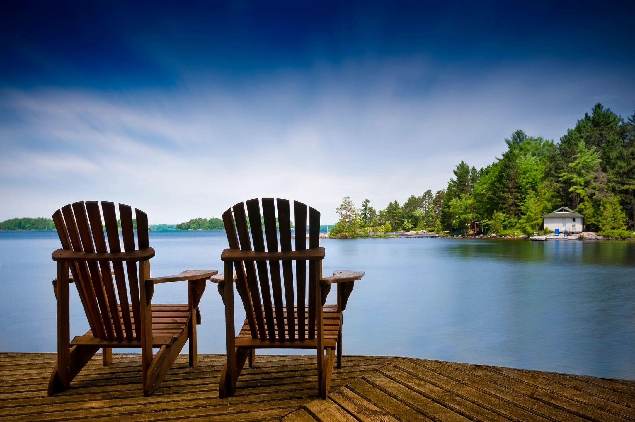 Two wooden chairs on a deck overlooking the water.